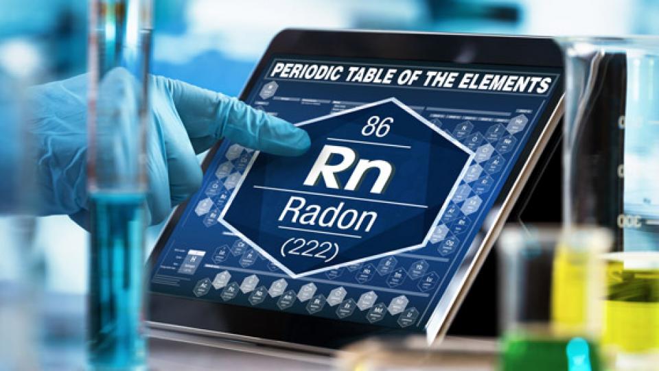 Eine Hand zeigt auf ein Tablet, auf dem die chemische Formel für Radon (zusammegesetzt aus den Buchstaben Rn und der Ordnungszahl 86) abgebildet ist,