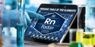 Eine Hand zeigt auf ein Tablet, auf dem die chemische Formel für Radon (zusammegesetzt aus den Buchstaben Rn und der Ordnungszahl 86) abgebildet ist, 
